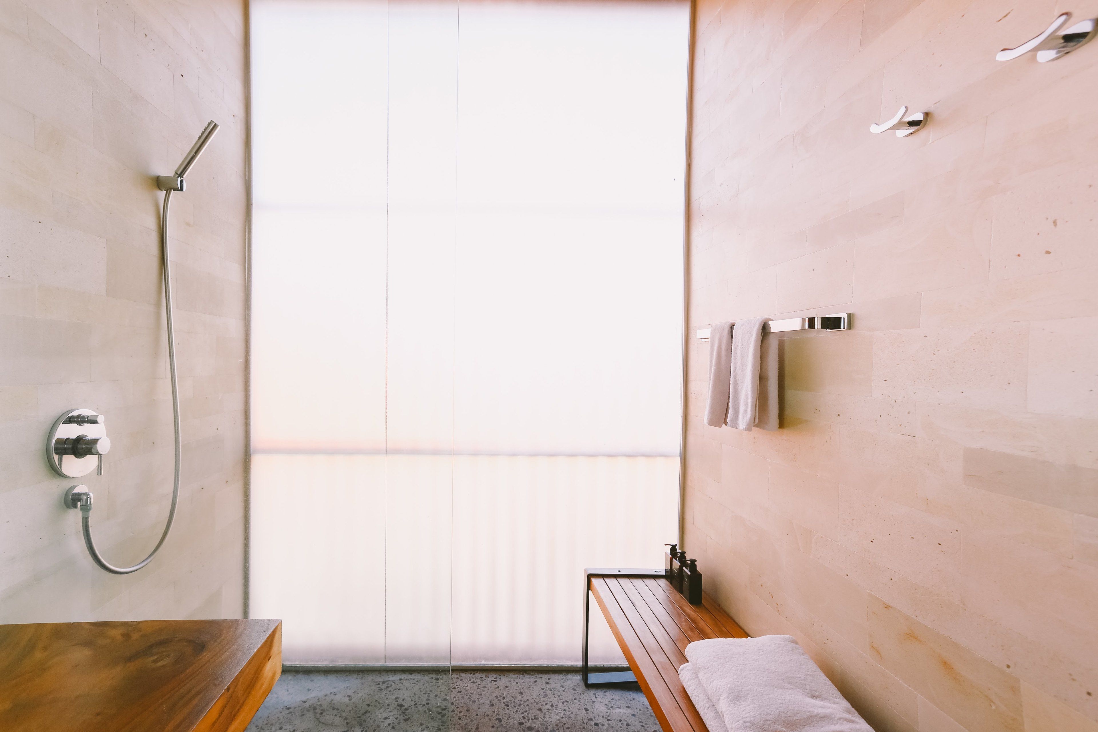 Een moderne badkamer met een houten bankje, een douche en een handdoekhouder.