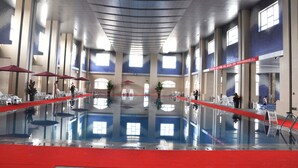 A large indoor swimming pool with a red border, surrounded by white chairs and red umbrellas. - Country Garden Phoenix Hotel, XingAnMeng (Xing'an)