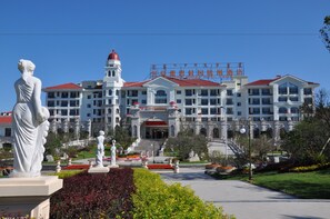 A large hotel with multiple floors, a central entrance, and a statue in the foreground.
