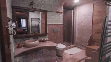 A bathroom with a stone wall, a sink, a toilet, and a shower.