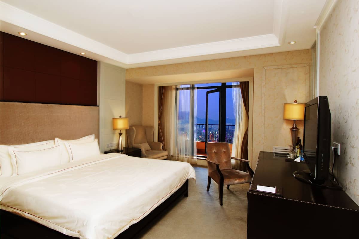 Une chambre d’hôtel avec un grand lit, un bureau avec une télévision et une chaise.