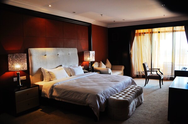 A spacious bedroom with a large bed, a nightstand, a chair, and a desk.