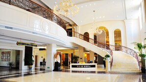 Eine geräumige Lobby mit Marmorboden, einer imposanten Treppe und einem Kronleuchter.