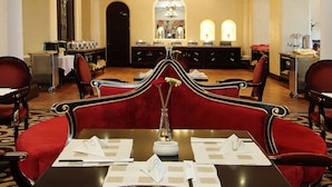 Ein Hotel-Essbereich mit roten, gepolsterten Stühlen, einem schwarzen Tisch mit Speisekarten und einer Kristallleuchter.