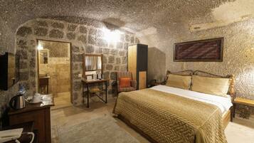 A stone-walled bedroom with a bed, a desk, a chair, a mirror, and a framed tapestry.