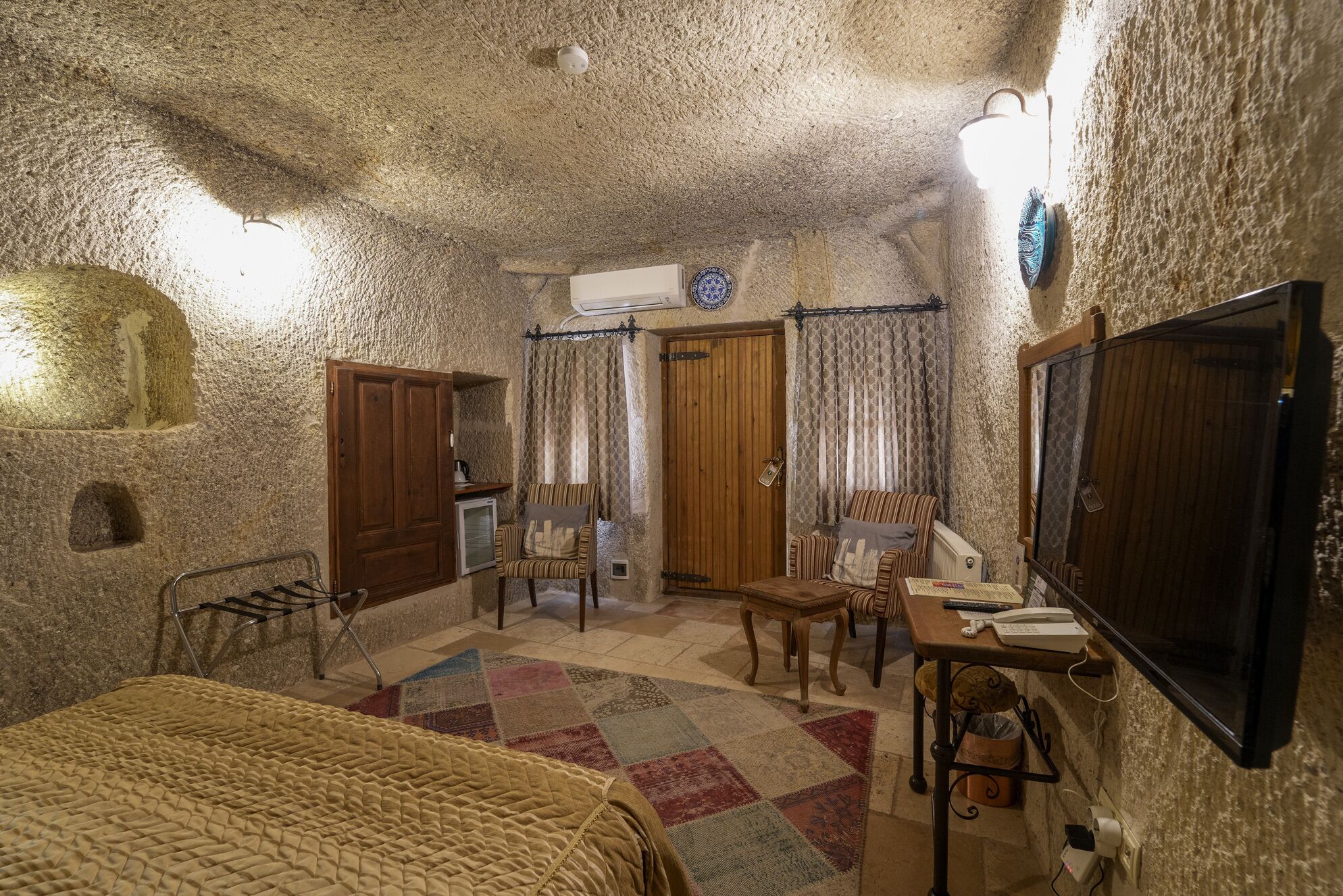 A cozy room with a bed, a small table with a chair, a television, and a window with curtains.