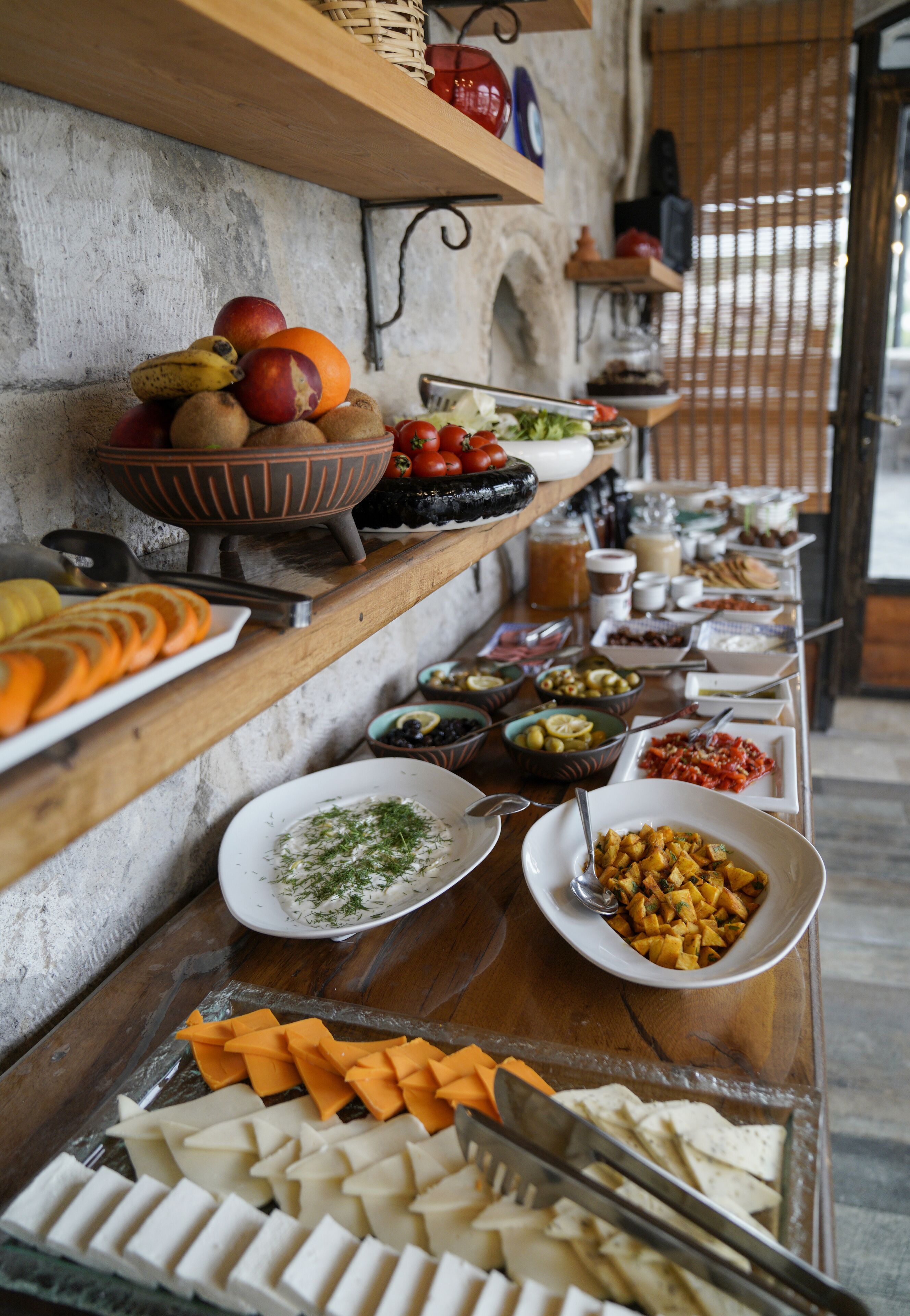 A buffet with various food items and a wooden shelf with fruits.