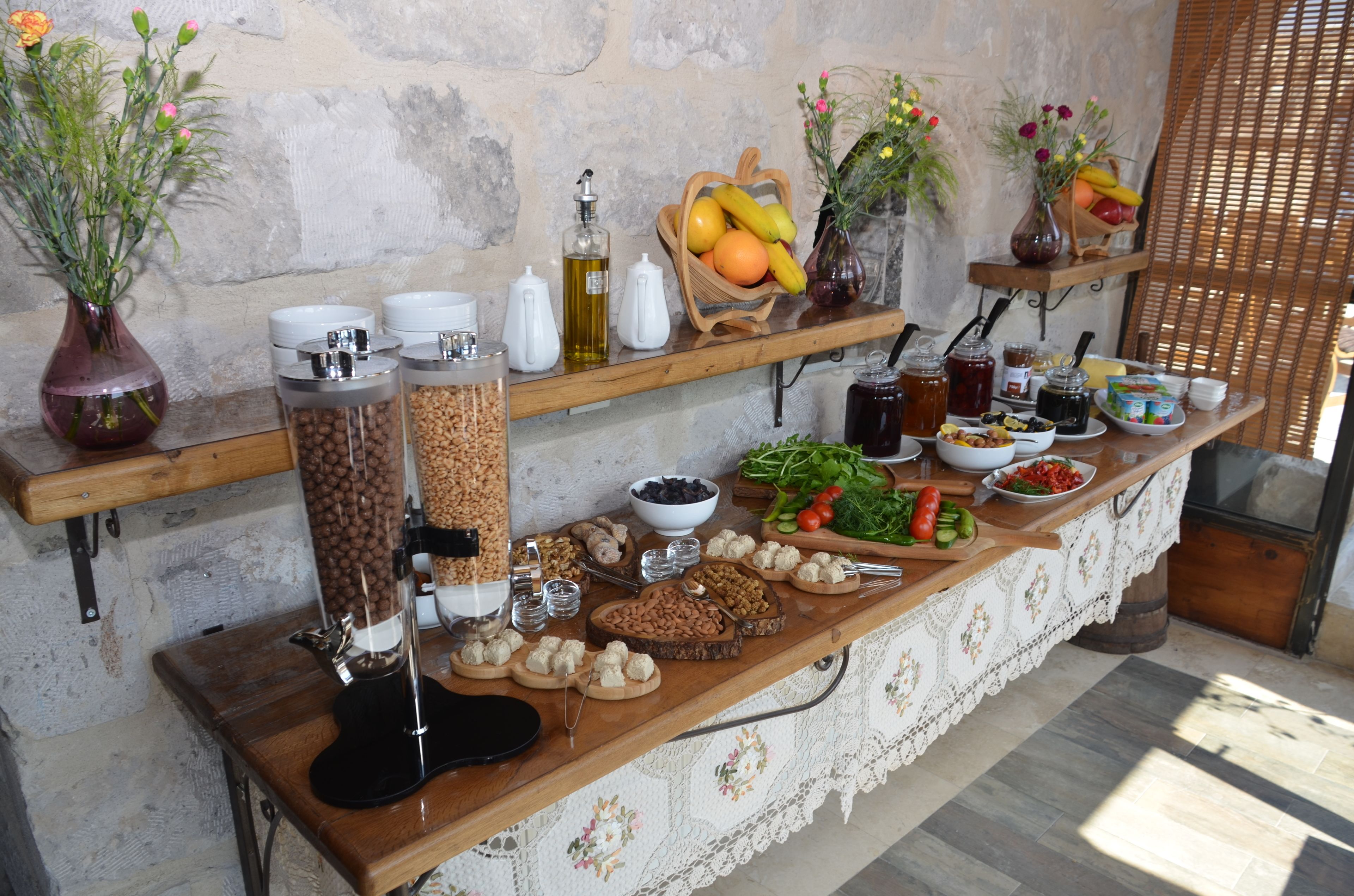 A buffet setup with various food items and condiments on wooden tables against a stone wall.