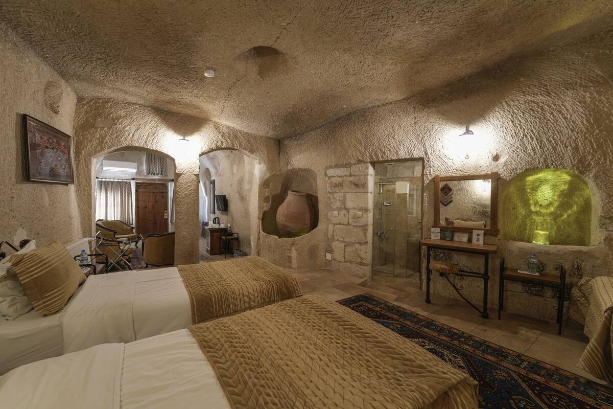 Habitació rústica amb dos llits, una paret de pedra, una porta de fusta i un mirall amb un objecte verd.