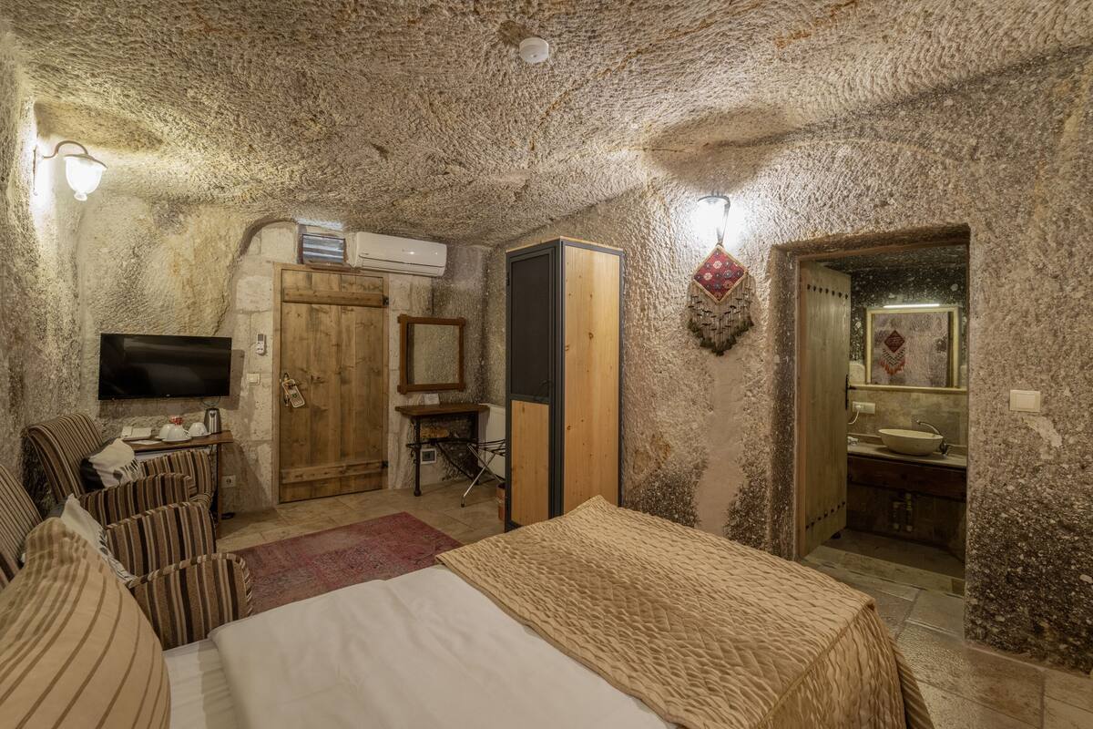 Habitació rústica amb un llit, una televisió, un armari de fusta, un mirall i un banyet petit.