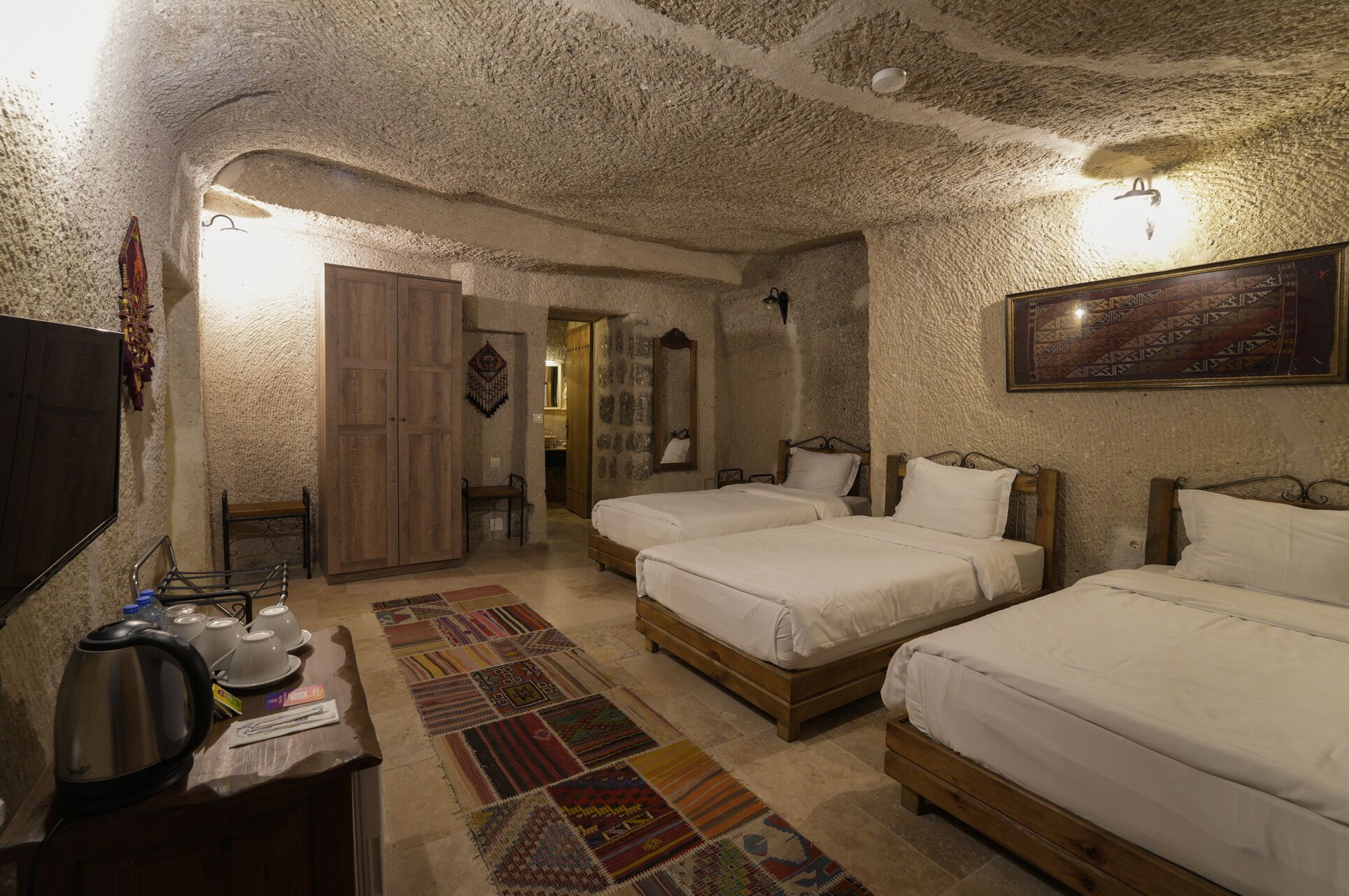 A room with two wooden beds, a wooden wardrobe, a small table with a kettle, and a patterned rug.