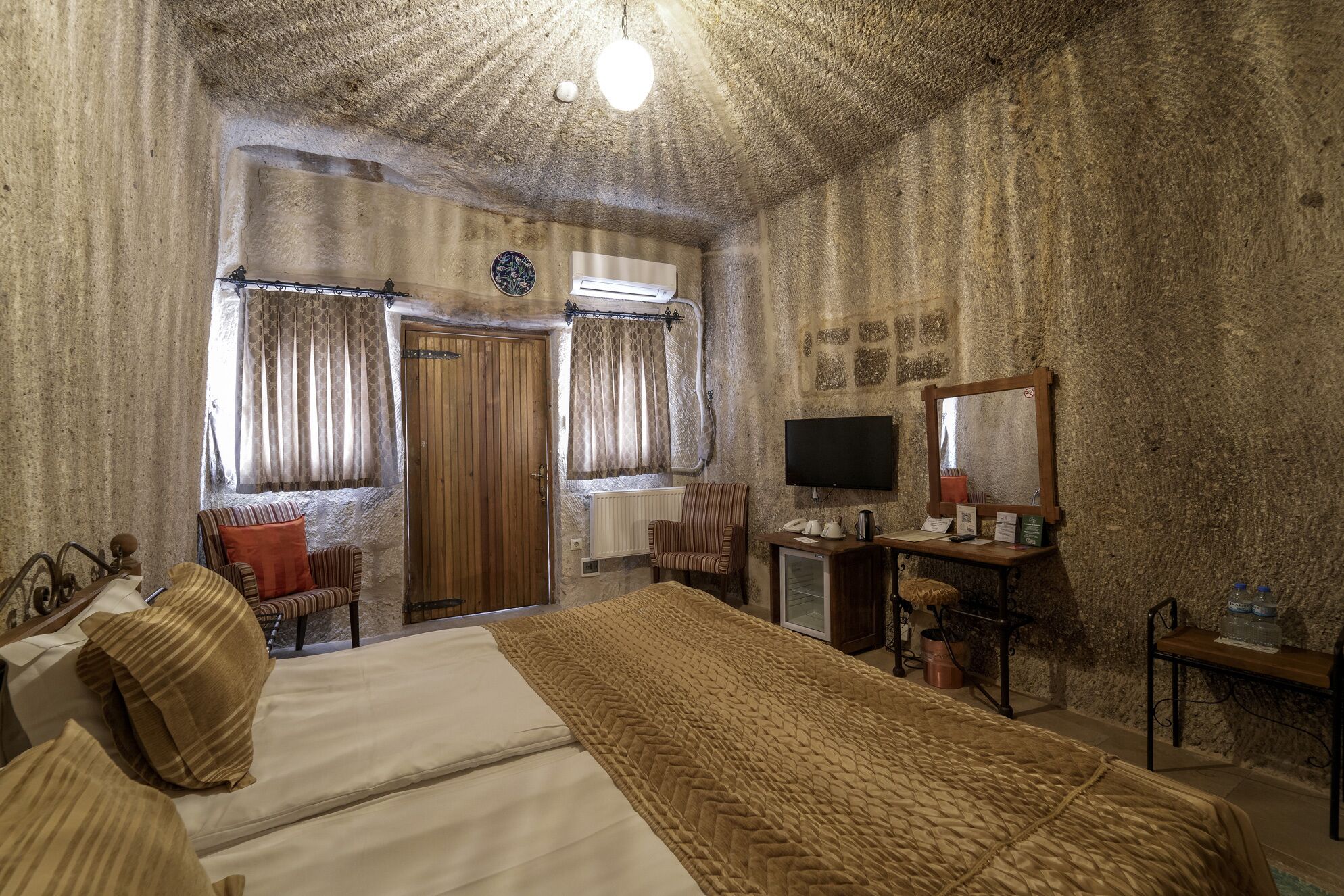 Una habitación con una cama, un escritorio con computadora, una silla, un televisor y un espejo.