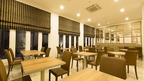Un interior de restaurante moderno con varias mesas y sillas, ventanas grandes con cortinas a rayas y ventiladores de techo.