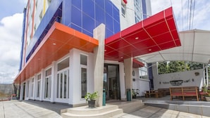 Un edificio moderno con fachada roja y azul, un área de entrada cubierta con asientos y un letrero que dice "TERAS & KOPI".