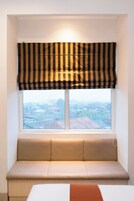 A window with a striped valance, a cushioned bench, and a view of a residential area.