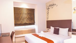 Habitación de hotel con cama, escritorio, silla, ventana con persianas y decoración en la pared.