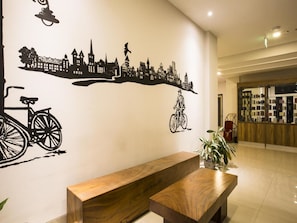 A reception area with a wooden bench, a cityscape wall art, and a plant. - Sparks Odeon Sukabumi - Artotel Curated (Sukabumi)