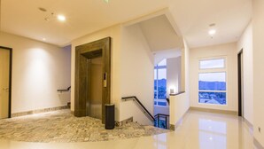 Un pasillo amplio y luminoso con piso pulido, una puerta grande y una escalera que sube a un nivel superior.