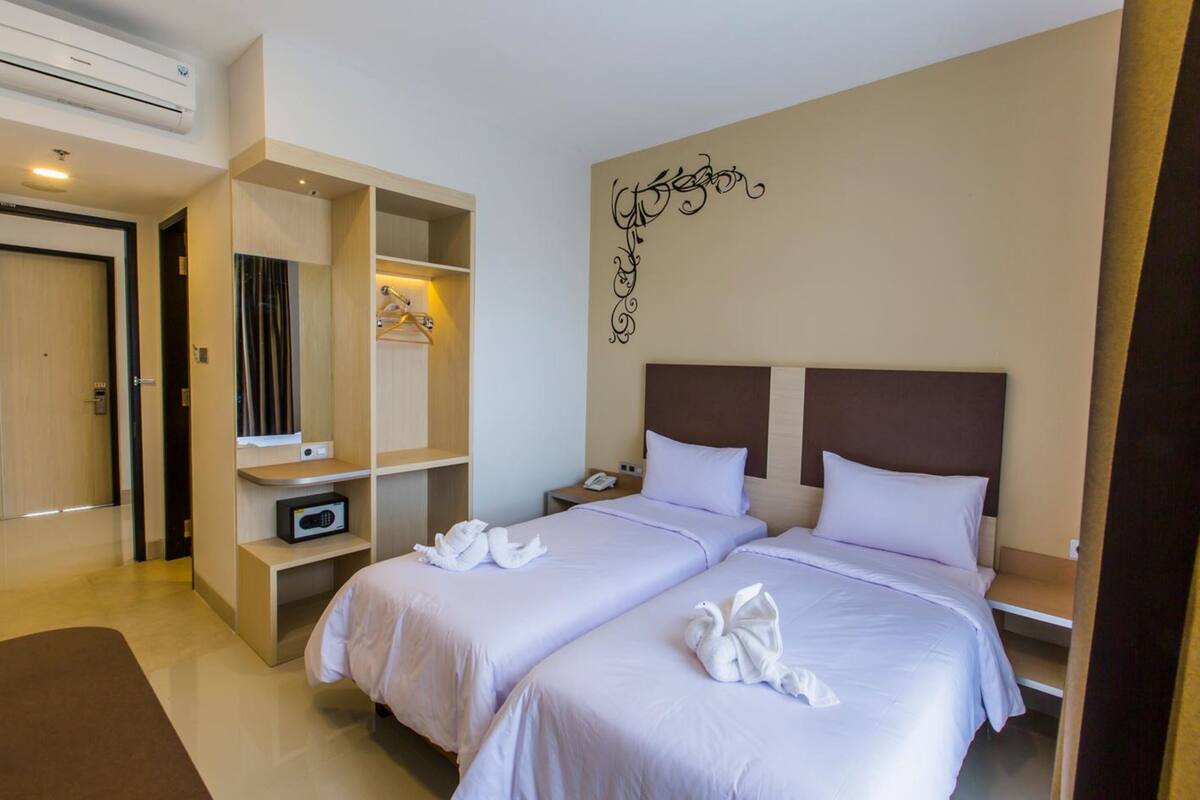 A hotel room with two beds, a wardrobe, a desk, and a wall decoration.