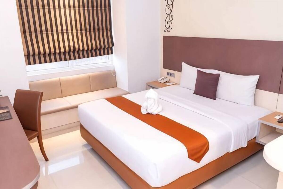 A hotel room with a bed, bedside table, chair, desk, and window with curtains.