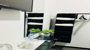 A modern bathroom with a black and white color scheme, a glass partition, a sink with toiletries, and two potted plants. - House Of Seya (Negombo)