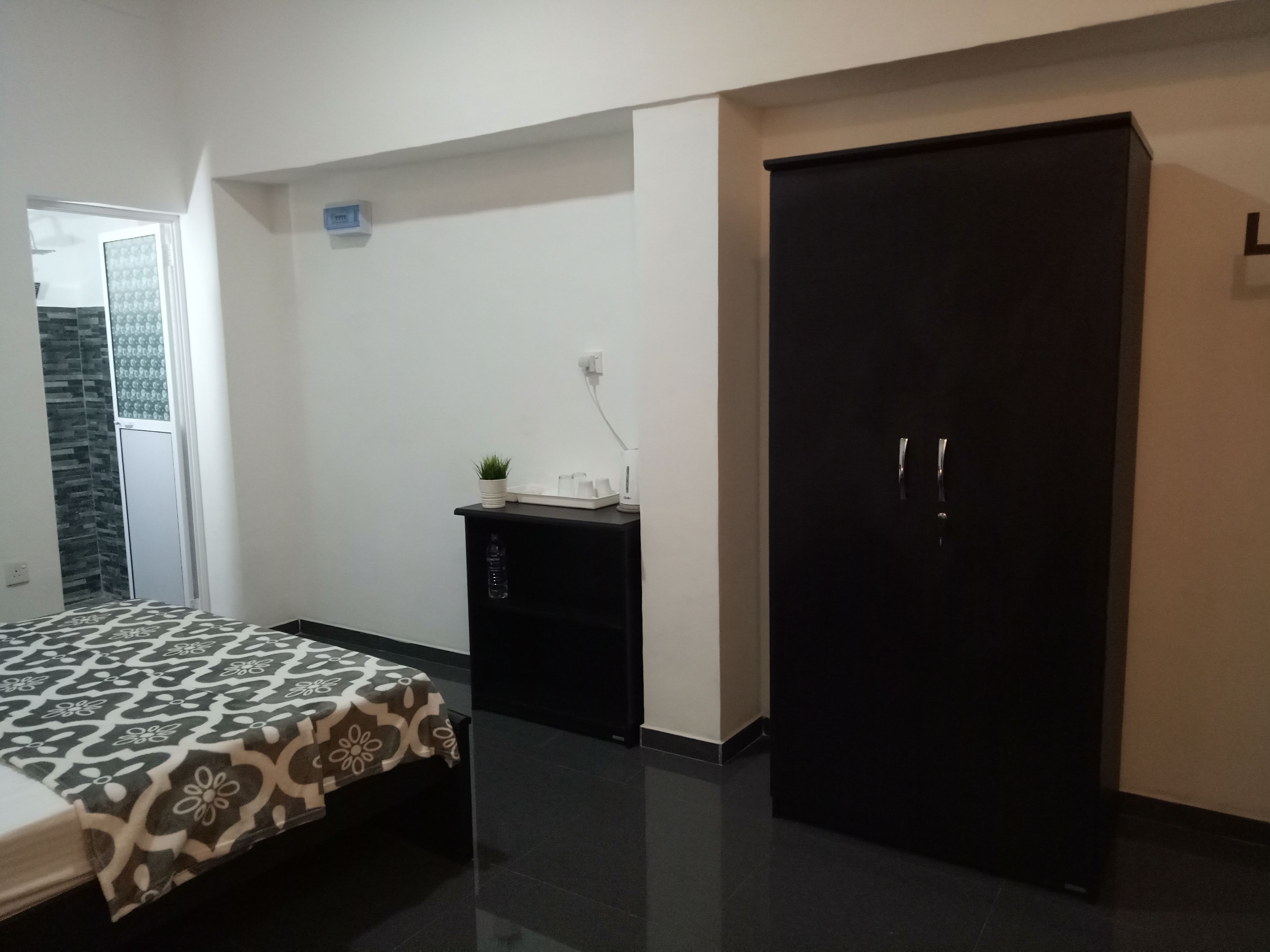 A bedroom with a bed, a wardrobe, a small table with a plant, and a wall-mounted outlet.
