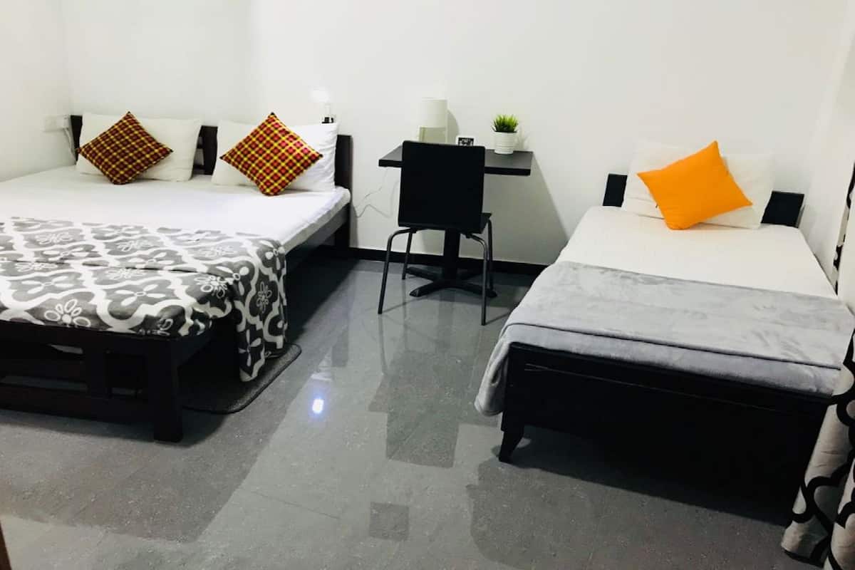 A small, clean room with two beds, a desk, and a chair.