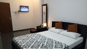 Una habitación de hotel con una cama, un televisor montado en la pared, una mesita de noche con una lámpara y un espejo.