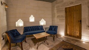 Una habitación con puerta de madera, un sofá azul, dos sillones azules, una mesa de centro de madera y una alfombra estampada.