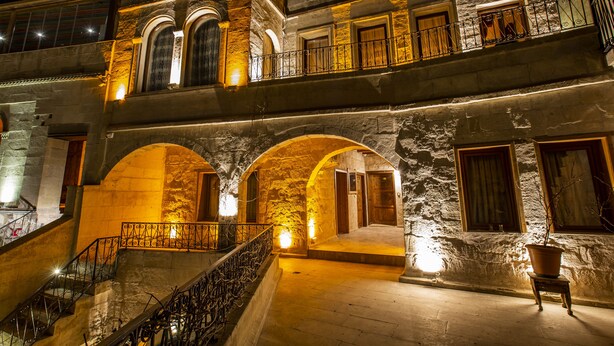 Un edificio de piedra de varios niveles con escaleras abovedadas y balcones, iluminado con una luz cálida.