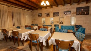 Un comedor con mesas y sillas de madera, un sofá azul y una araña.