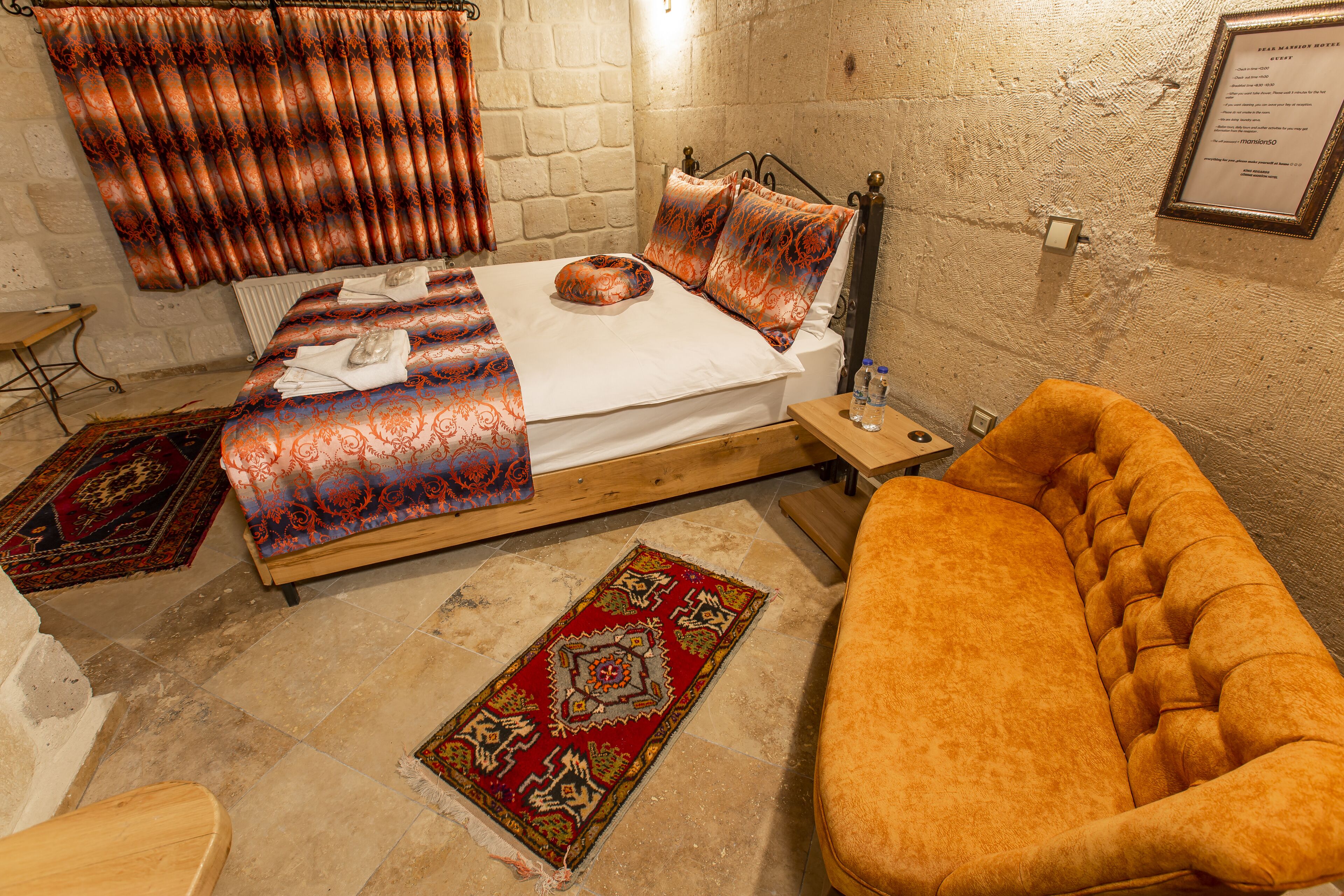 A room with a bed, a wooden nightstand, a sofa, and a red patterned rug.