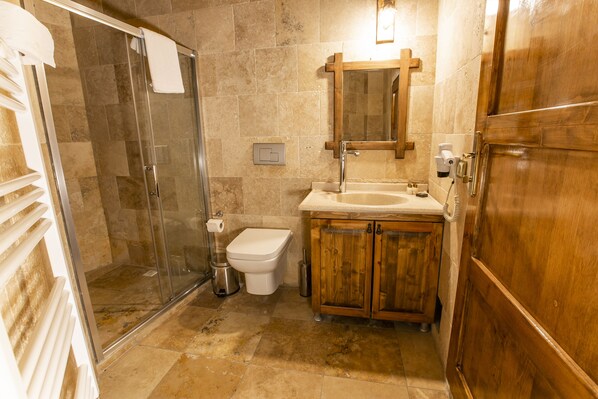 Baño con cabina de ducha de vidrio, inodoro, lavabo con armarios de madera y espejo sobre el lavabo.