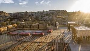 Una terraza en la azotea con un conjunto de sofás, una mesa de comedor y vistas a un paisaje montañoso.