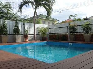 A swimming pool with a wooden deck, surrounded by a white fence, with potted plants and a palm tree. - Baan Par Pern Hadchaosamran (Phetchaburi)