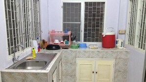 Una pequeña cocina con un lavamanos, una ventana con barrotes, un refrigerador y un microondas.