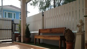 Un patio con un banco de madera, plantas en macetas y una valla blanca.