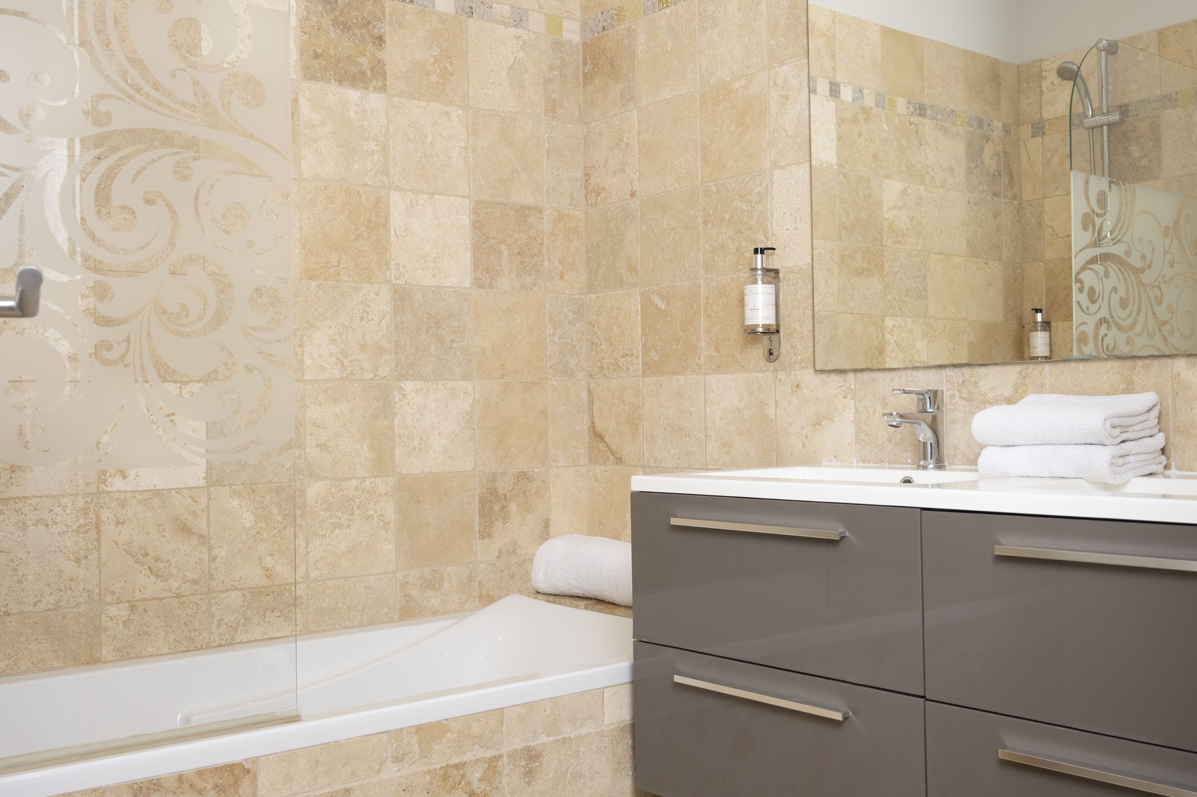 A bathroom with beige tiles, a white bathtub, a sink with a mirror, and a towel rack.