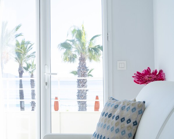 Una habitación con un ventanal grande, una pared blanca y vistas a palmeras y un balcón.