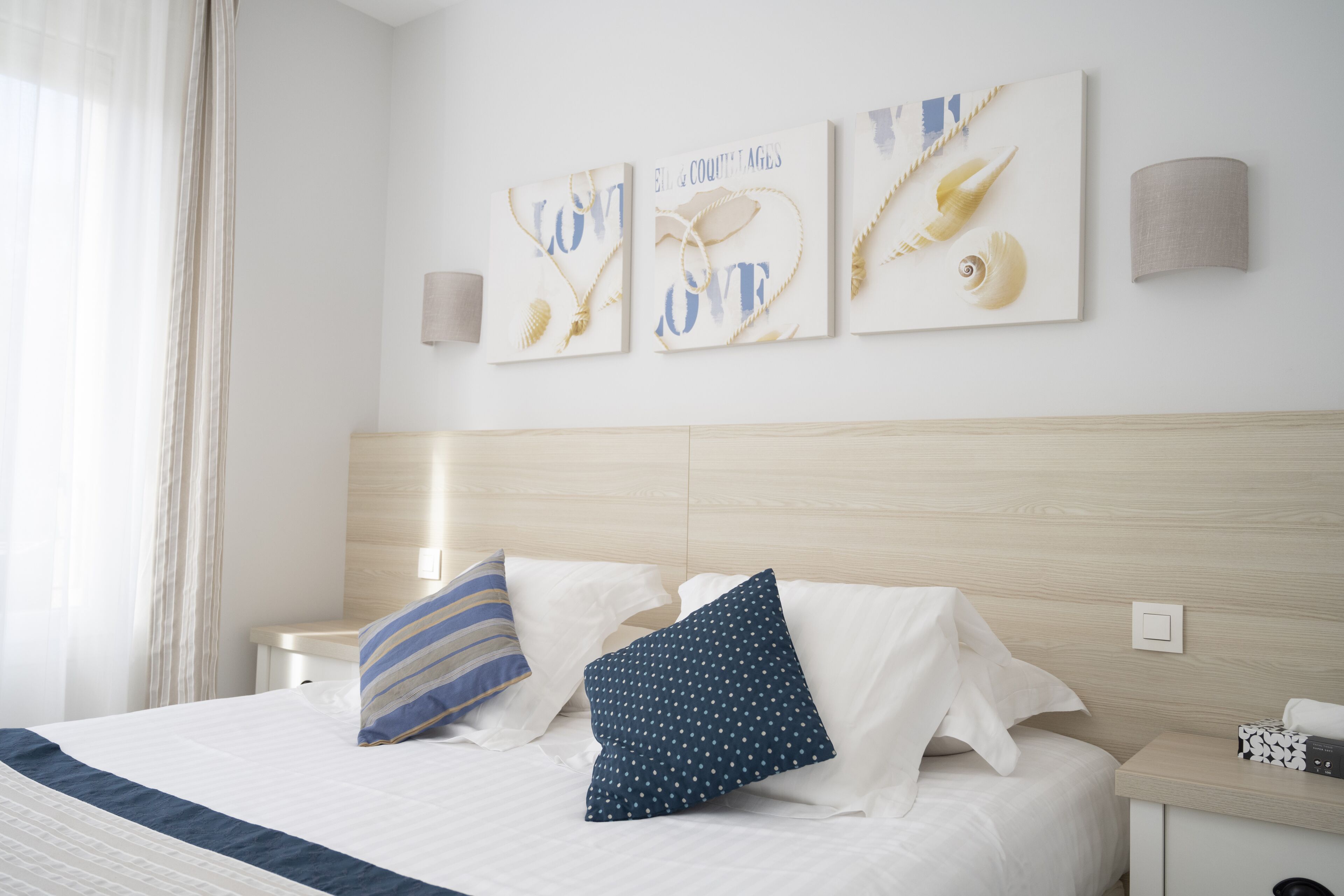 Una cama bien hecha con almohadas blancas y azules, un cabecero de madera y tres piezas decorativas con motivos náuticos.