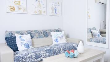 A modern living room with a sofa, pillows, and a coffee table. There are three framed artworks on the wall and a mirror above the coffee table.