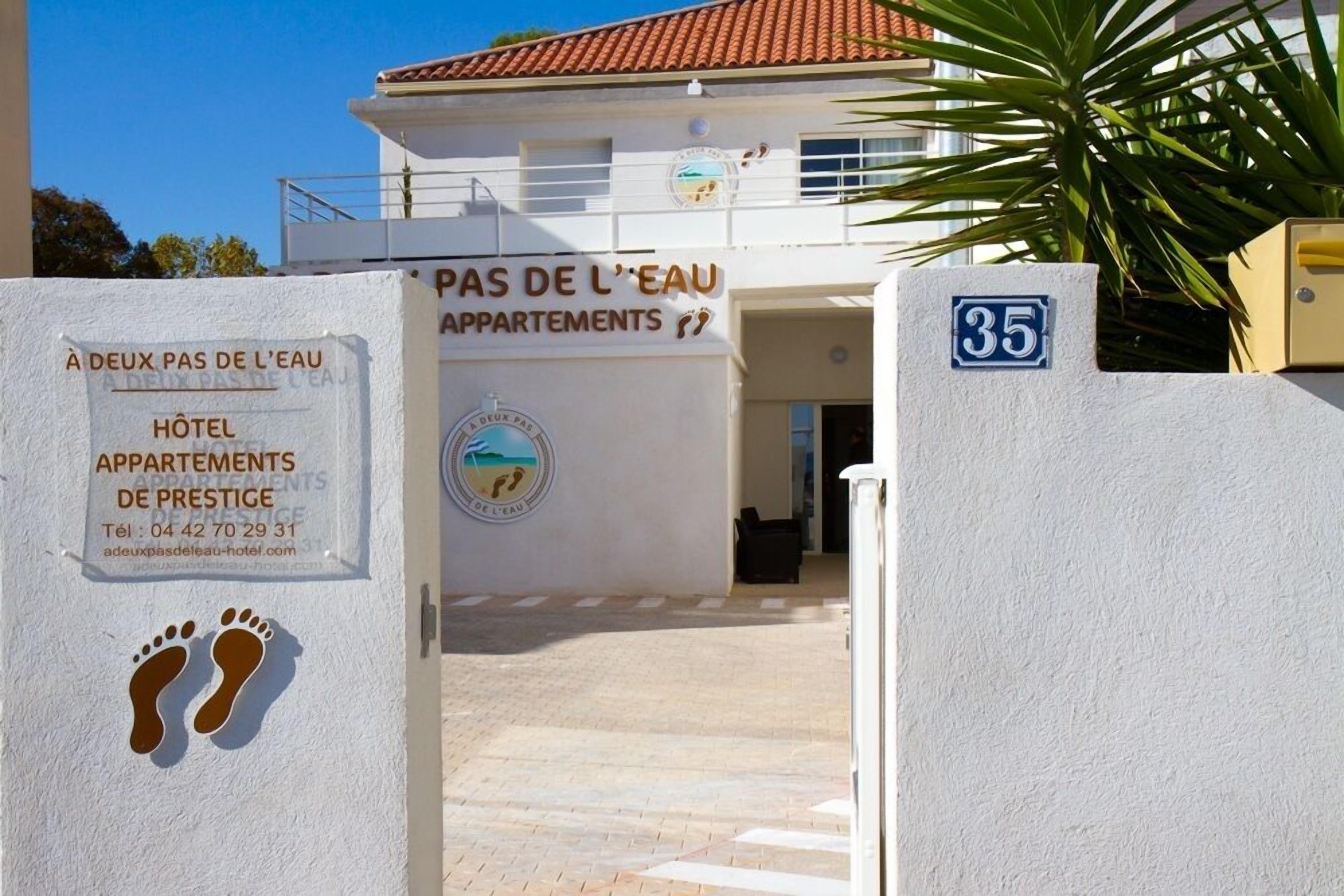 A building with a sign reading "Hôtel Appartements de Prestige" and a logo with a beach and footprints.