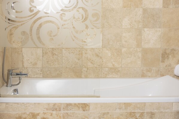 Un baño con bañera, ducha y una pared con azulejos decorativos.