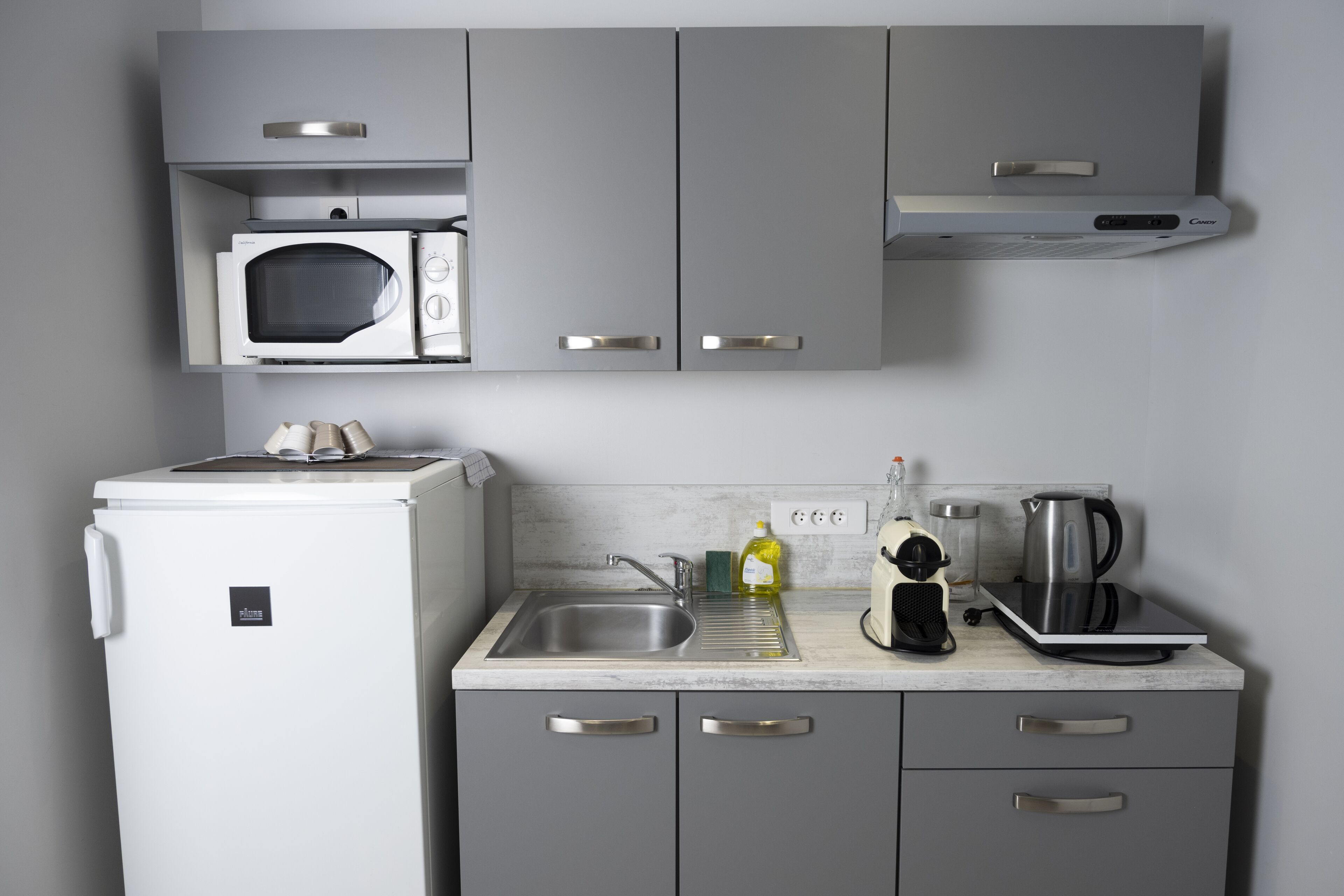 A compact kitchen with a microwave, coffee maker, and kettle on the countertop.