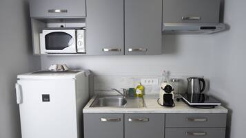 A compact kitchen with a microwave, coffee maker, and kettle on the countertop.