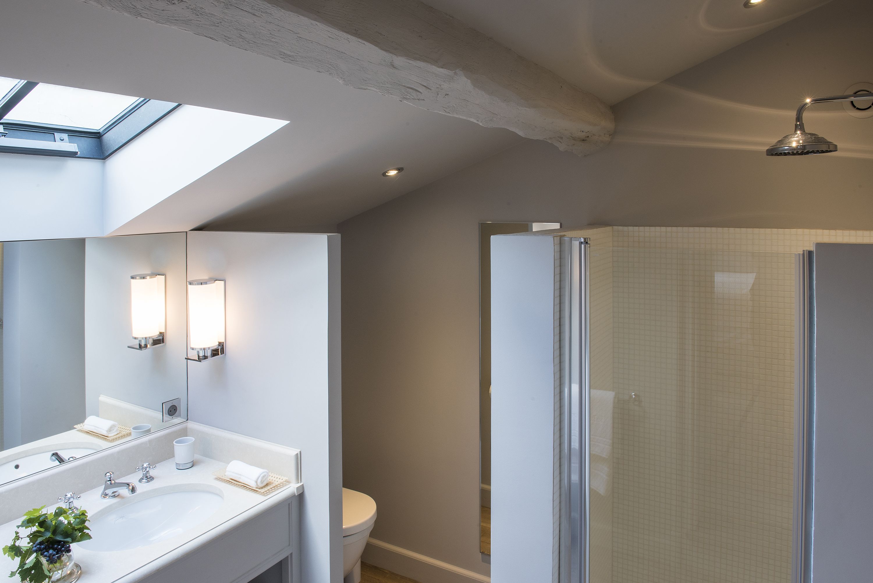A modern bathroom with a skylight, a large mirror, a double sink, and a glass-enclosed shower.