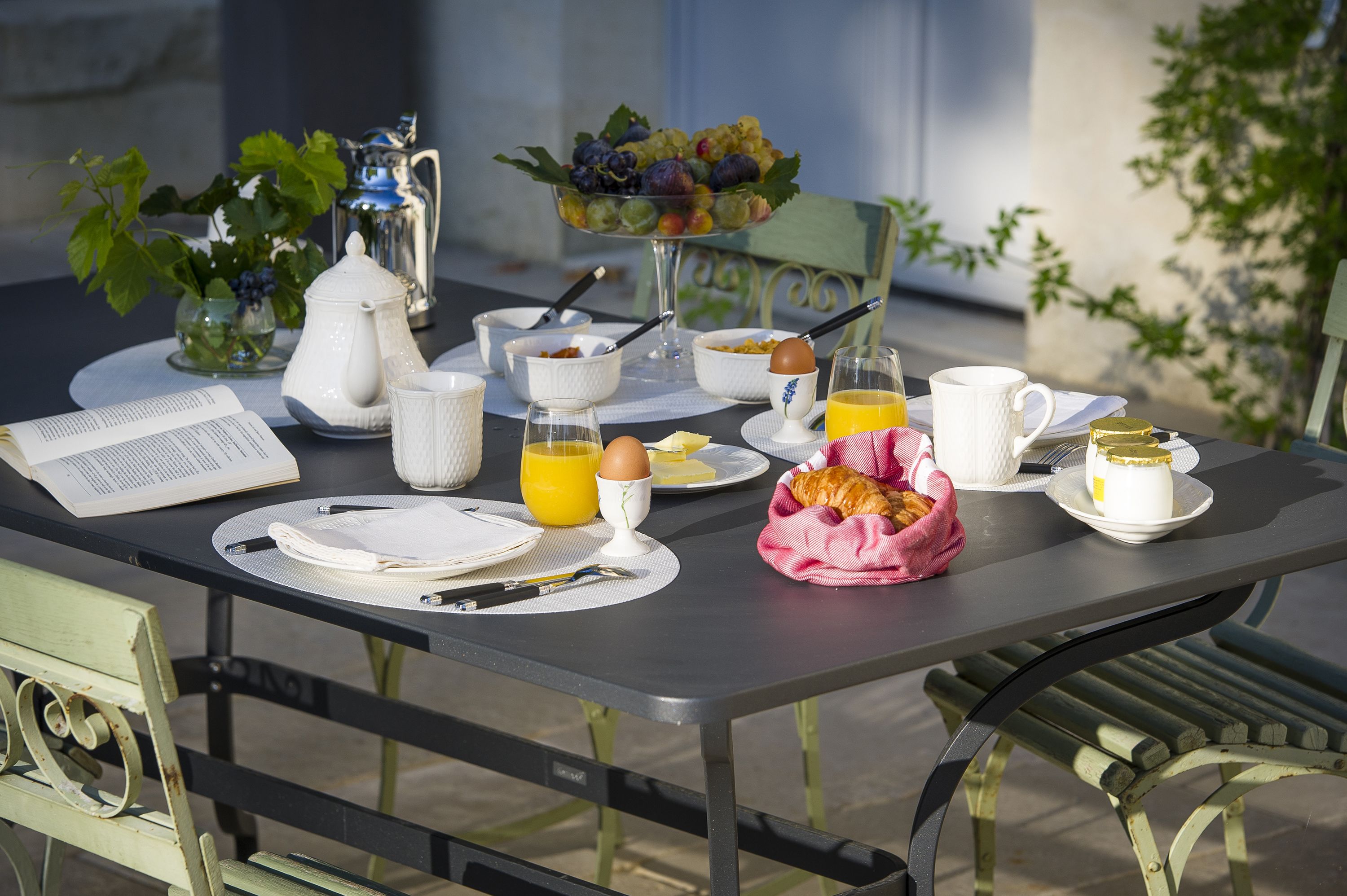 Una mesa de desayuno con una jarra, tazones, un libro y una cesta de fruta.