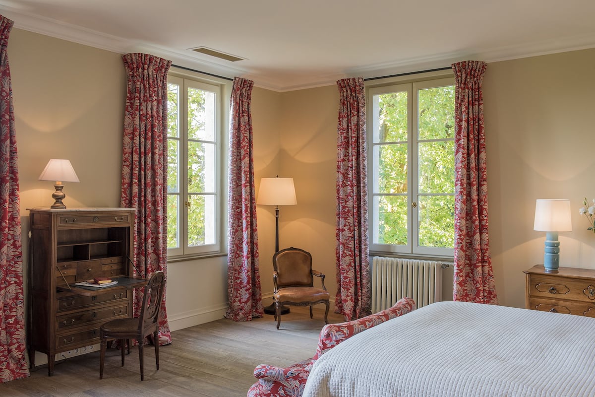 A bedroom with a bed, a desk, a chair, and two lamps.