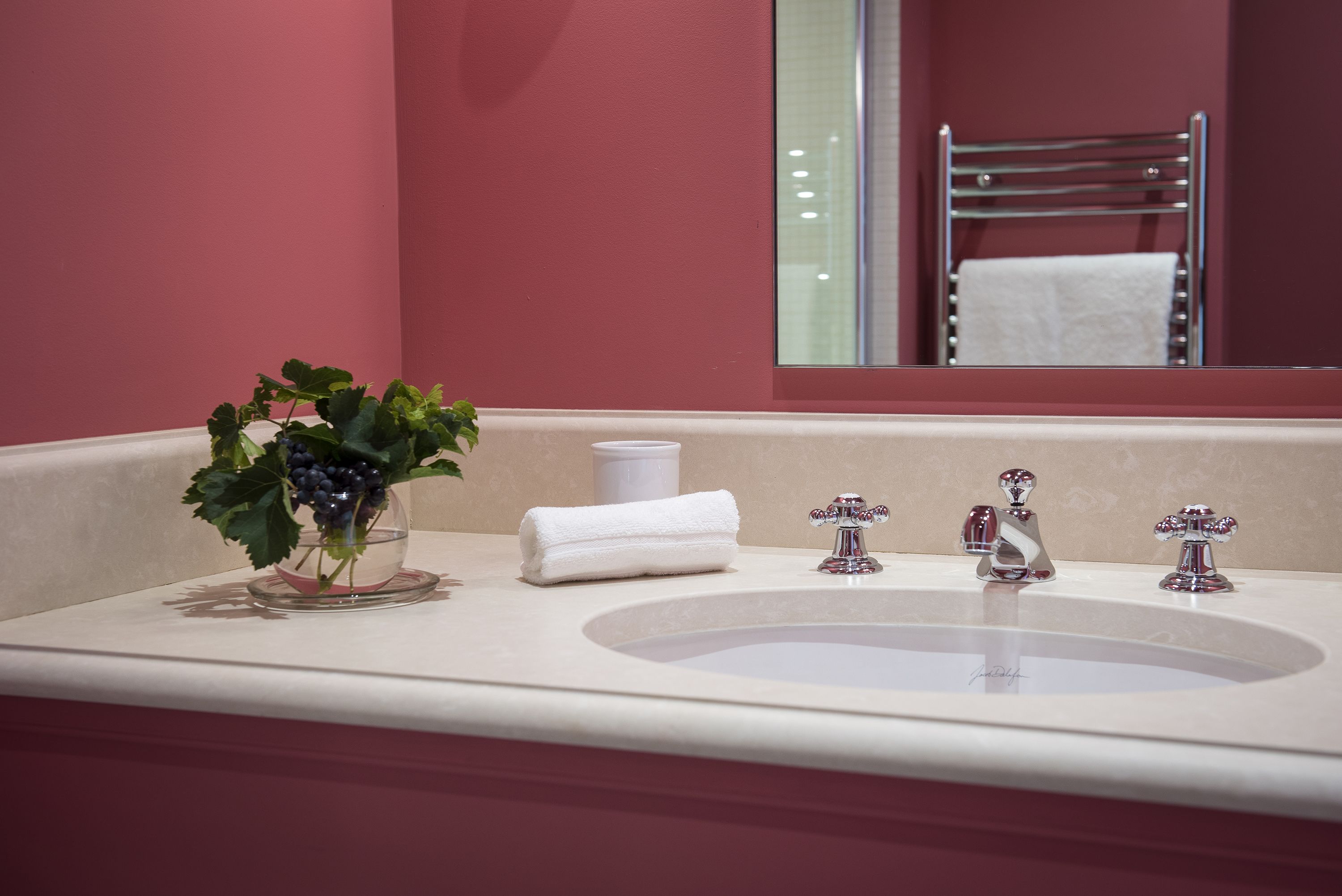 Ein Badezimmer mit einem weißen Waschbecken, zwei Chromarmaturen, einem weißen Handtuch und einer Glasvase mit grünen Blättern.