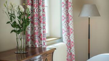 A wooden dresser with a vase of white flowers, patterned curtains, and a floor lamp in a room.